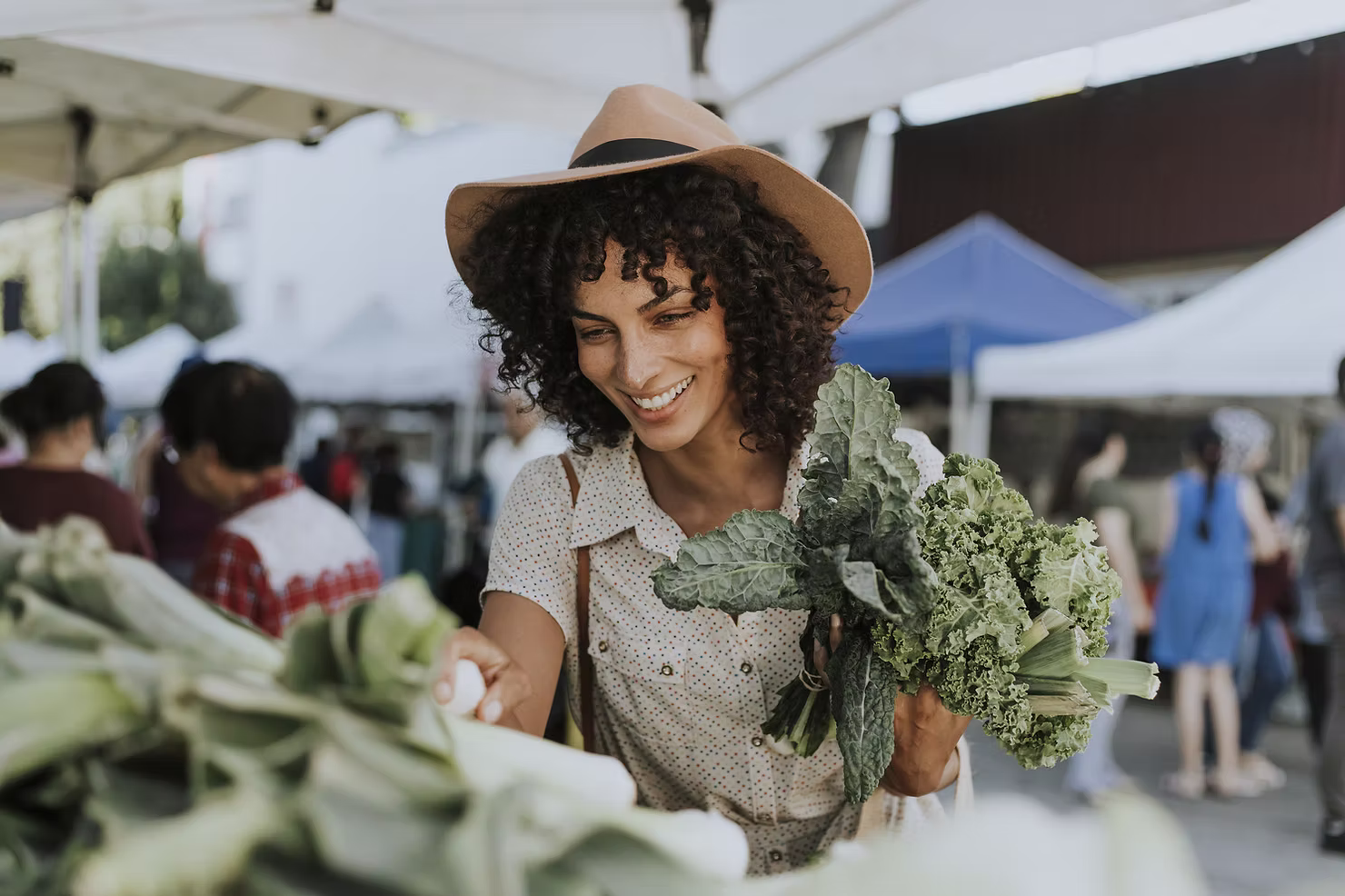 A shopper holding leafy vegetables at an outdoor farmers market