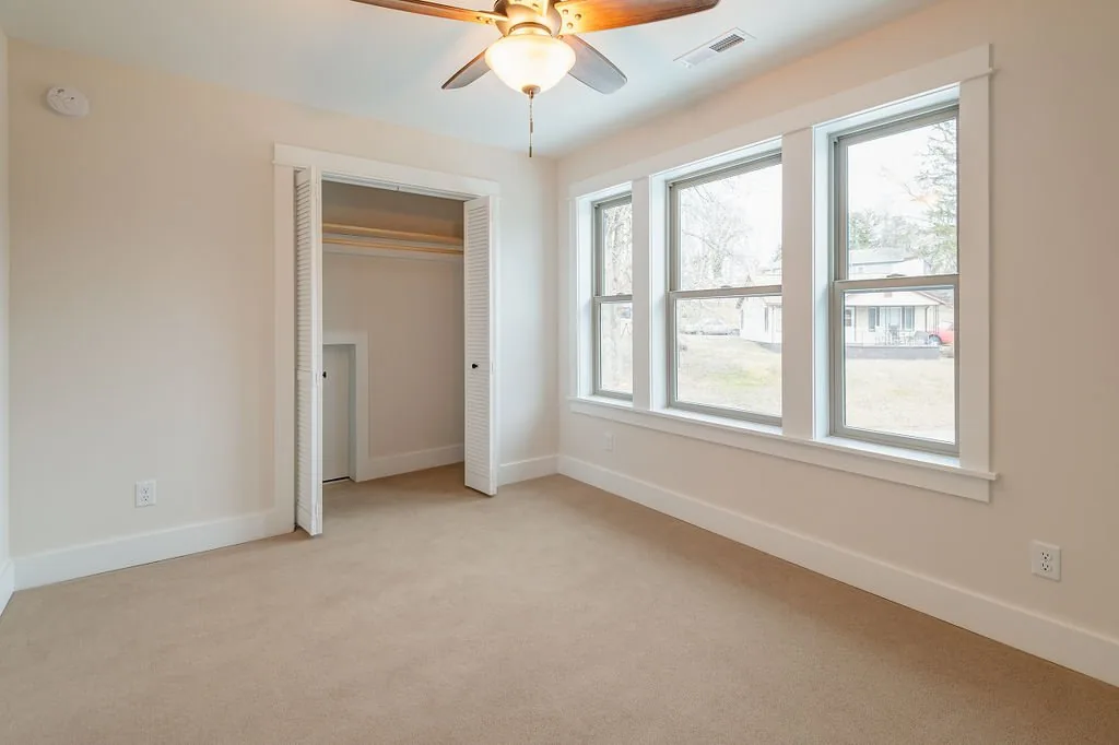 Carpeted bedroom with three windows and a closet